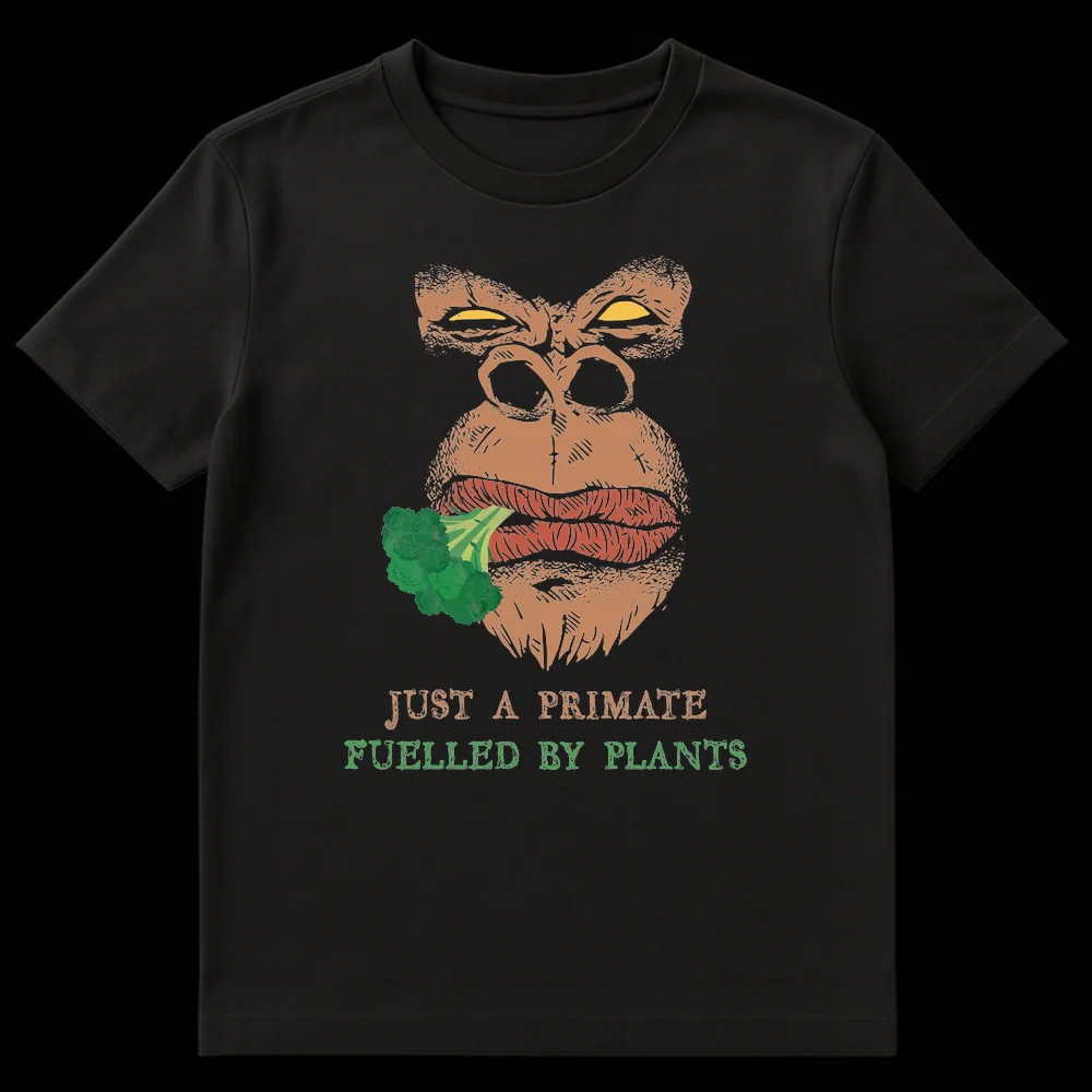Distressed comic style graphic t-shirt featuring an intense gorilla eating broccoli with text 'JUST A PRIMATE FUELLED BY PLANTS' in tan and green colors. on Black t-shirt