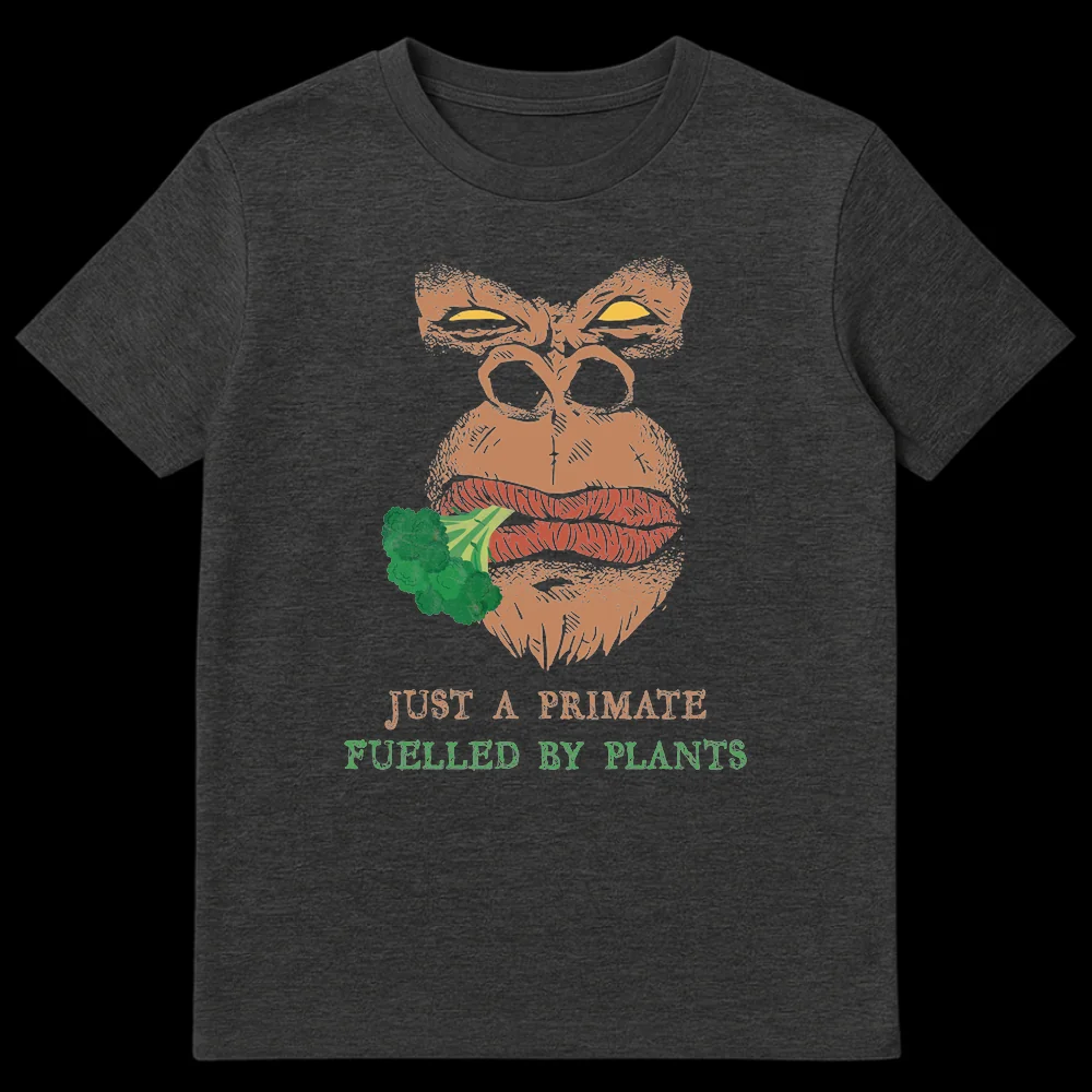 Distressed comic style graphic t-shirt featuring an intense gorilla eating broccoli with text 'JUST A PRIMATE FUELLED BY PLANTS' in tan and green colors. on Dark Heather t-shirt