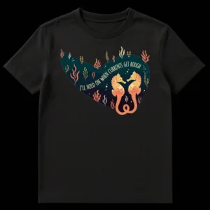 Two golden and coral seahorses with intertwined tails in a heart shape, surrounded by seaweed, on a dark teal t-shirt with text 'I'LL HOLD ON WHEN CURRENTS GET ROUGH' on Black t-shirt