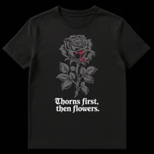 T-shirt with 'Thorns first, then flowers.' text and a graphic of a bleeding rose on a thorny stem, symbolizing resilience and life's journey. on Black t-shirt