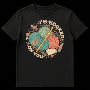 I'M HOOKED ON YOU crochet t-shirt design featuring pastel yarn, a crochet hook, and an open craft book on a black background. on Black t-shirt